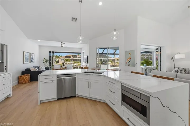 Kitchen with open floor plan, light stone counters, stainless steel appliances, lofted ceiling, and white cabinets