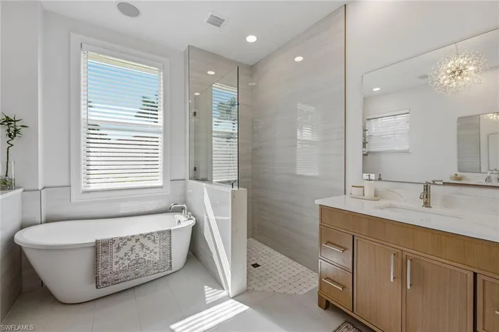 Bathroom featuring vanity, a freestanding bath, walk in shower, plenty of natural light, and tile walls