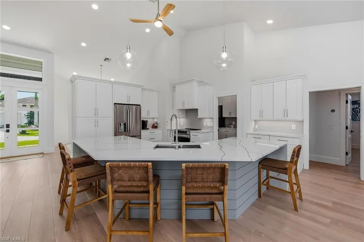 Kitchen with a ceiling fan, white cabinets, a breakfast bar area, a large island, and stainless steel appliances