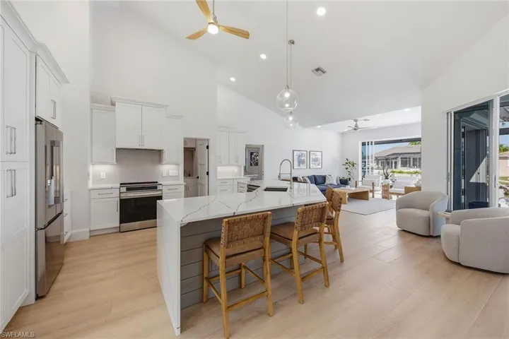 Kitchen featuring ceiling fan, white cabinets, stainless steel appliances, open floor plan, and lofted ceiling