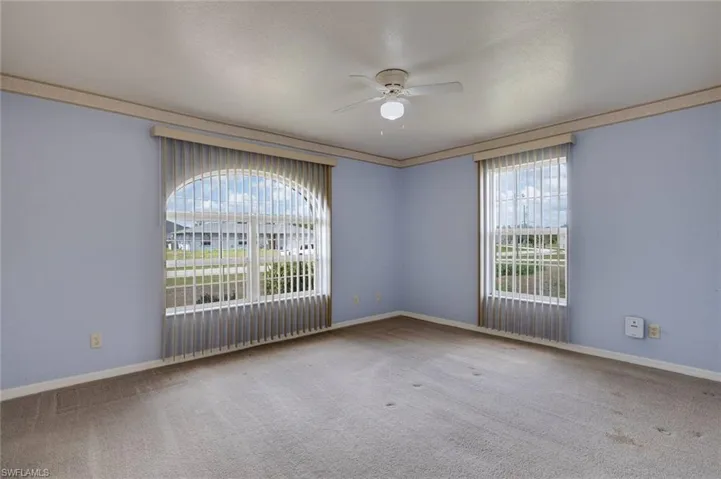 Empty room featuring a ceiling fan, light carpet, ornamental molding, and a textured ceiling