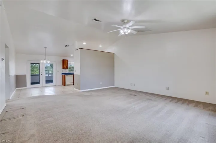 Unfurnished living room featuring hanging lights, lofted ceiling, light carpet, and ceiling fan
