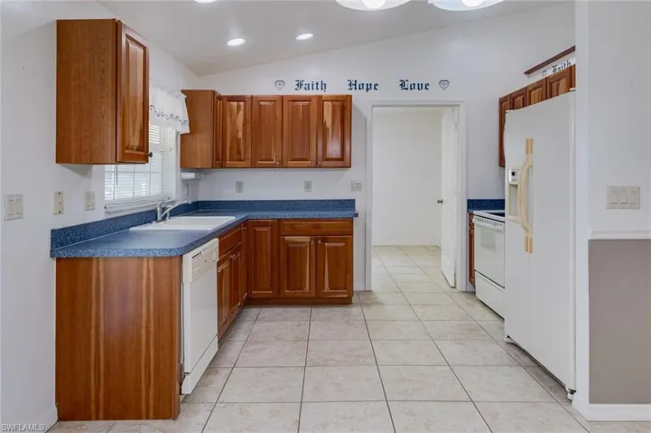 Kitchen with wood finish cabinetry, dark countertops, lofted ceiling, white appliances, and light tile patterned floors