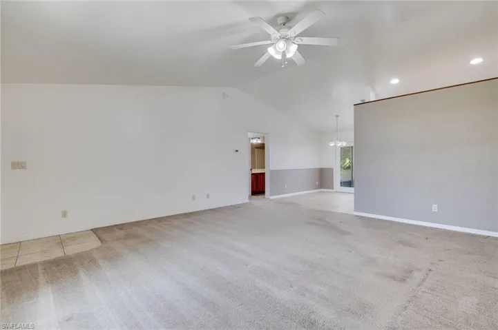 Empty room featuring lofted ceiling, ceiling fan, light colored carpet, and a chandelier