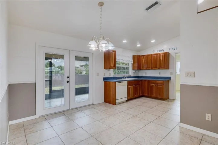 Kitchen featuring wood finish cabinets, vaulted ceiling, a chandelier, white dishwasher, and french doors
