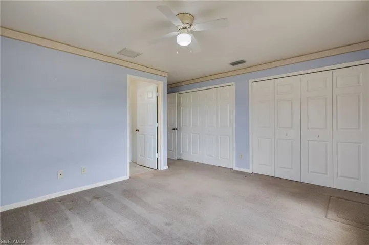 Unfurnished bedroom featuring multiple closets, light colored carpet, and a ceiling fan