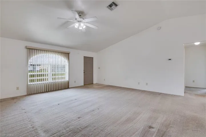 Spare room featuring ceiling fan, vaulted ceiling, and light carpet