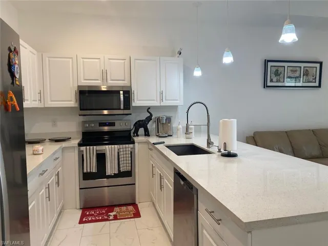 Kitchen with marble finish floor, a peninsula, white cabinets, a sink, and stainless steel appliances