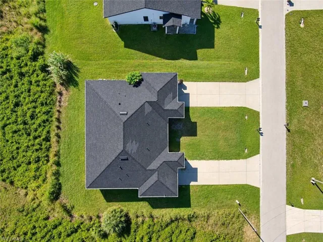 Aerial view featuring a multi-gabled shingle roof, concrete driveway, and expansive lawn area