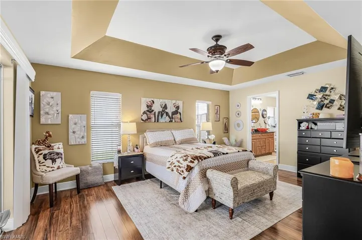 Bedroom featuring dark wood-style flooring, a tray ceiling, ceiling fan, and ensuite bathroom
