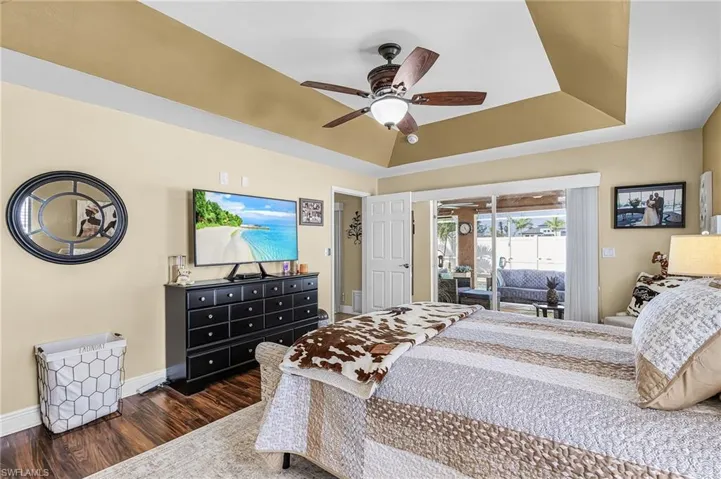 Bedroom with a raised ceiling, dark wood-style flooring, access to exterior, and ceiling fan