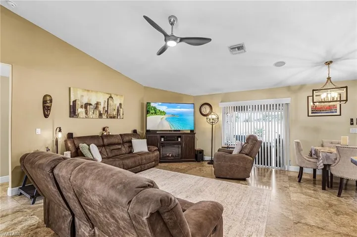 Living area with a ceiling fan, a glass covered fireplace, vaulted ceiling, and suspended lighting