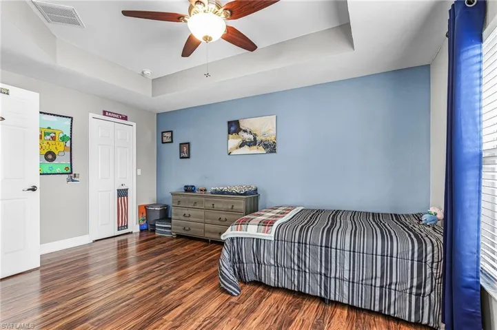 Bedroom featuring a tray ceiling, dark wood-style flooring, a ceiling fan, and a closet