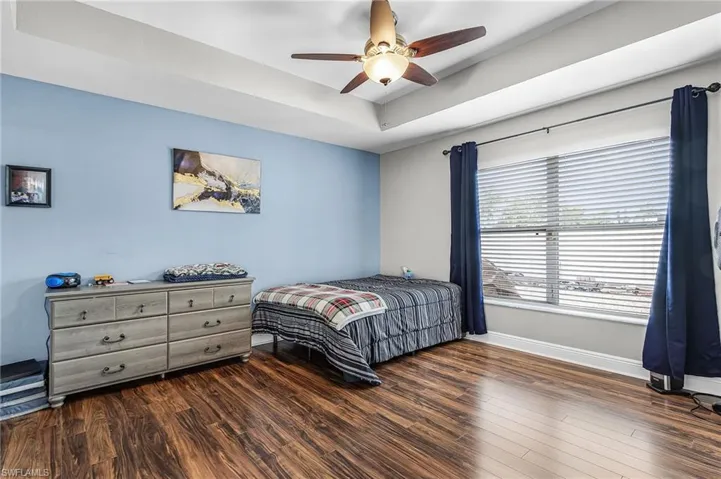 Bedroom with dark wood-style flooring, ceiling fan, and a raised ceiling