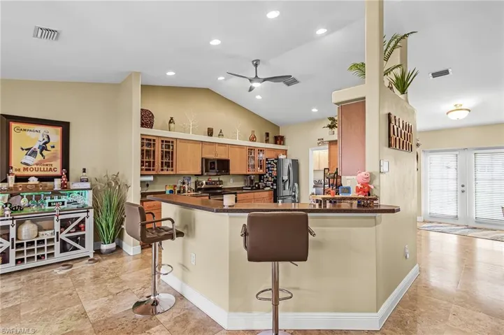 Kitchen featuring a breakfast bar area, glass insert cabinets, lofted ceiling, ceiling fan, and wood finish cabinetry