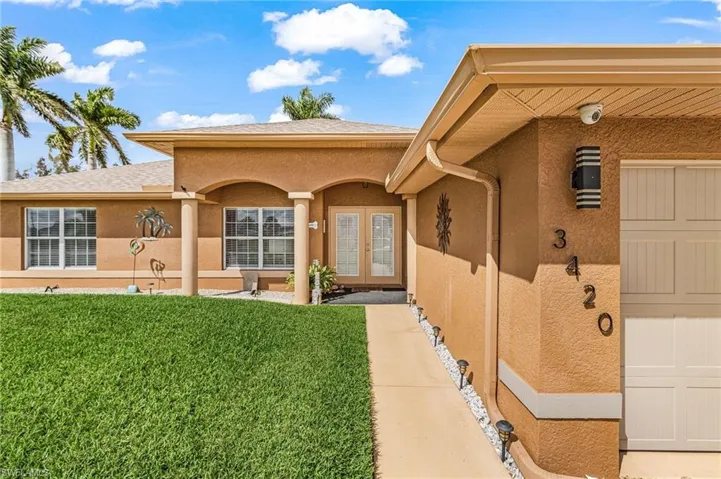 View of exterior entry featuring french doors, a lawn, stucco siding, a porch, and a shingled roof