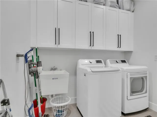Laundry area featuring white shaker-style cabinetry with matte black hardware, a utility sink with a chrome faucet, and tile flooring
