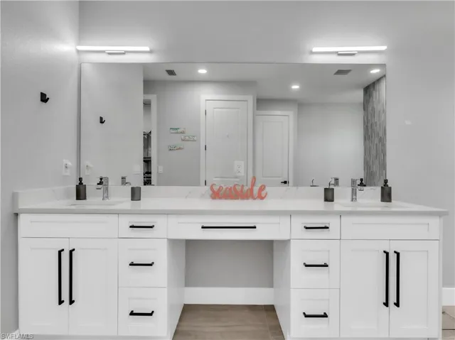 Dual-sink vanity featuring quartz countertops, white cabinetry with black hardware, and an integrated makeup area