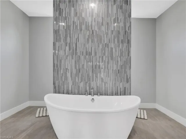 Freestanding oval bathtub with deck-mounted faucet, set against a full-height accent wall featuring vertical stacked mosaic tile