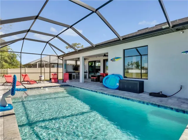 Screened-in outdoor living space featuring a rectangular swimming pool with a shallow entry, paver decking, and an outdoor kitchen area with built-in appliances