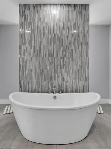 Freestanding soaking tub with polished chrome fixtures, set against a vertically-oriented mosaic tile accent wall