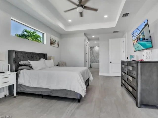 Spacious room featuring light-toned tile flooring, a tray ceiling with recessed lighting, and a ceiling fan