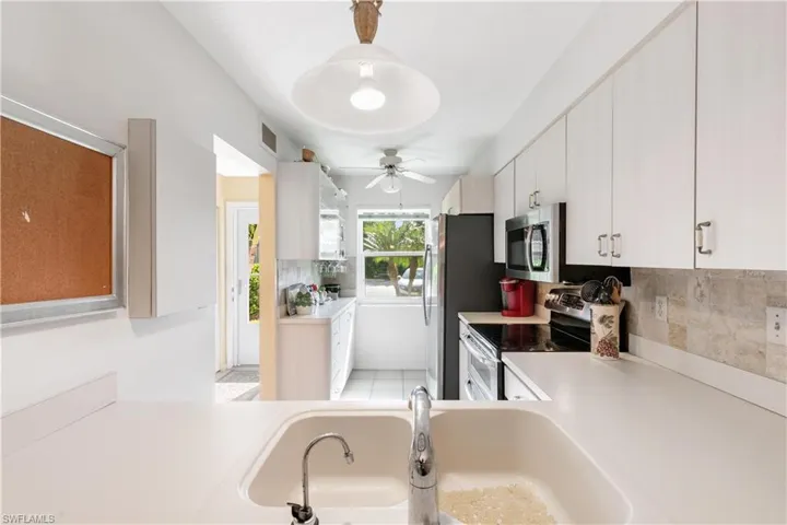Kitchen with stainless steel appliances, ceiling fan, tasteful backsplash, white cabinets, and sink