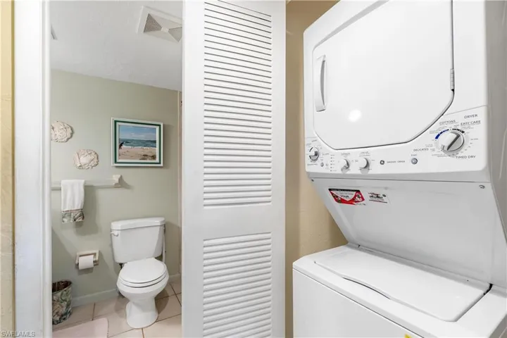 Washroom featuring stacked washing maching and dryer and light tile flooring