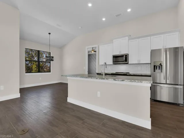 Kitchen featuring white cabinets, stainless steel appliances, a kitchen island with sink, vaulted ceiling, and backsplash