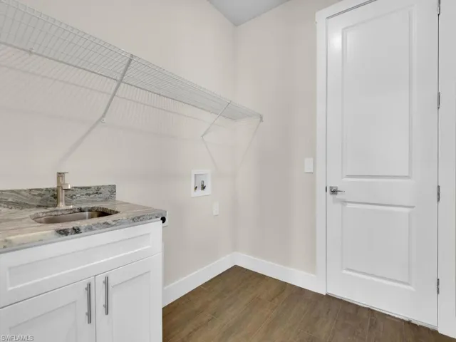 Laundry room with dark wood-style floors, washer hookup, baseboards, and a sink