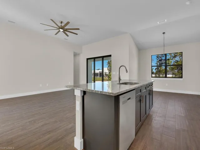Kitchen featuring stainless steel dishwasher, a sink, dark wood finished floors, open floor plan, and light stone countertops