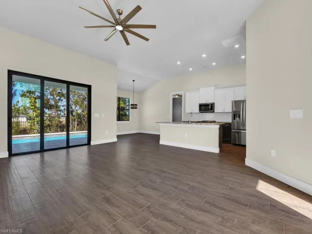 Unfurnished living room featuring dark wood-type flooring, a ceiling fan, baseboards, and recessed lighting