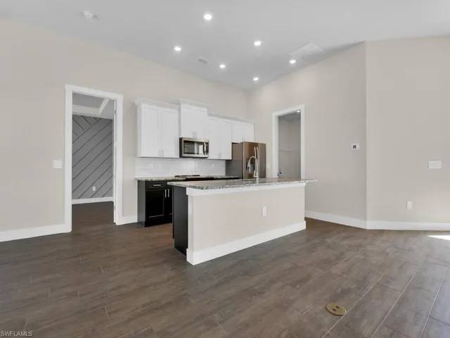 Kitchen featuring white cabinets, a kitchen island with sink, baseboards, backsplash, and appliances with stainless steel finishes