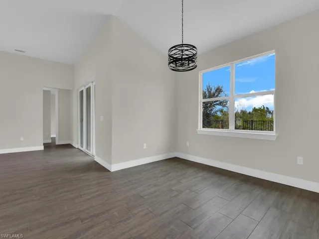 Spare room featuring dark wood-type flooring, baseboards, a notable chandelier, and vaulted ceiling