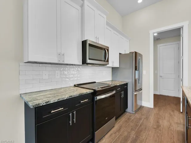 Kitchen with stainless steel appliances, backsplash, wood finished floors, light stone countertops, and white cabinetry