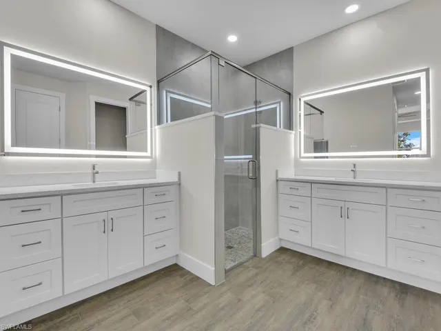 Bathroom with wood finished floors, two vanities, a sink, and a stall shower