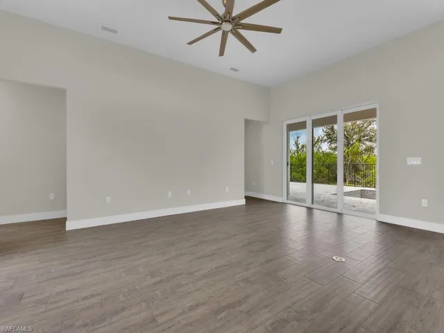 Empty room featuring ceiling fan, a high ceiling, baseboards, visible vents, and dark wood-style floors