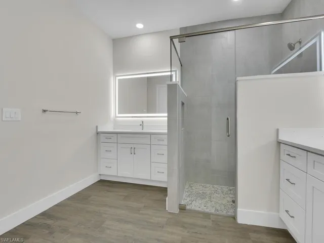 Bathroom with vanity, baseboards, a stall shower, and wood finished floors