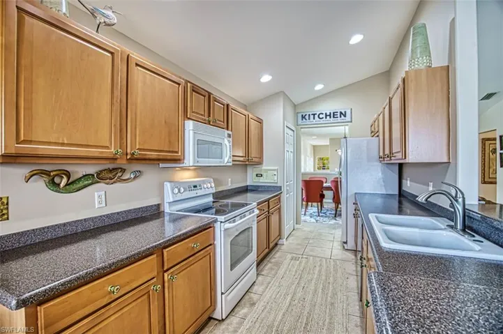 Kitchen featuring white appliances, vaulted ceiling, brown cabinetry, recessed lighting, and light tile patterned floors