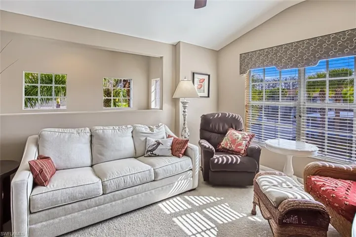 Living room with lofted ceiling, carpet flooring, and a ceiling fan