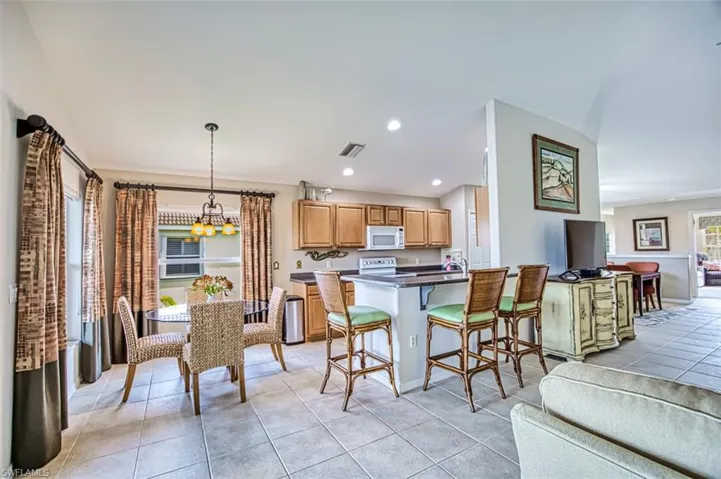 Kitchen with open floor plan, a breakfast bar, light tile patterned flooring, white appliances, and recessed lighting
