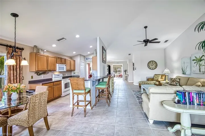 Kitchen with dark countertops, white appliances, vaulted ceiling, recessed lighting, and open floor plan
