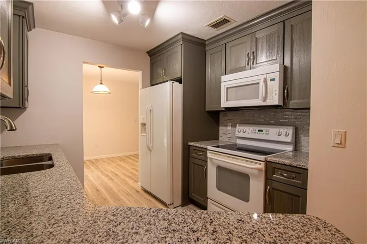Kitchen featuring white appliances, light stone countertops, backsplash, and light wood-style flooring