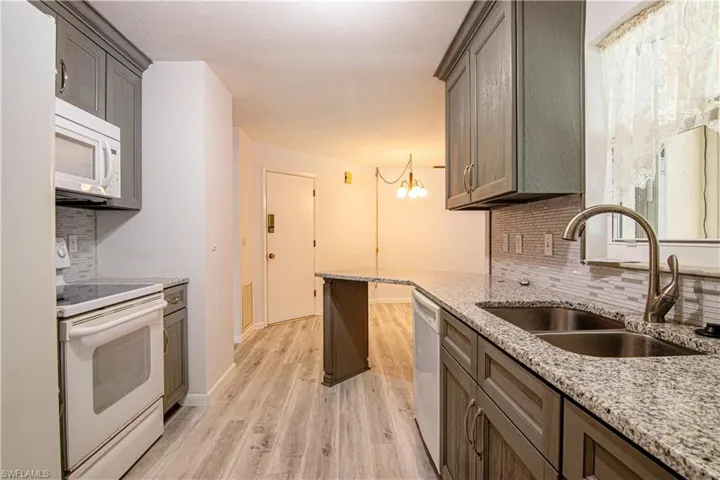 Kitchen with backsplash, white appliances, a chandelier, light wood-style floors, and light stone countertops