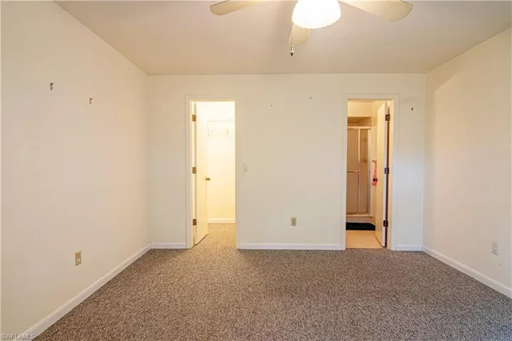 Unfurnished bedroom featuring light carpet, a ceiling fan, ensuite bath, and a spacious closet