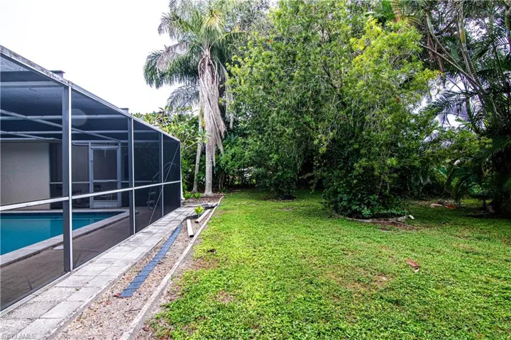 View of grassy yard with glass enclosure, a sunroom, an outdoor pool, and view of wooded area