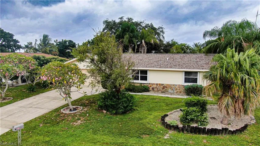 View of front of property featuring stone siding, concrete driveway, stucco siding, a front lawn, and a shingled roof
