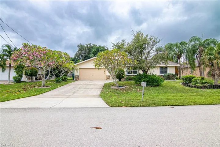 View of property hidden behind natural elements featuring concrete driveway, a front yard, stucco siding, and an attached garage