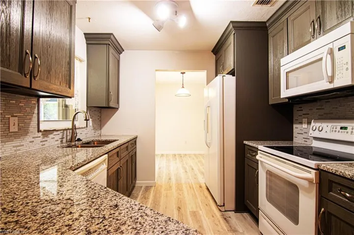 Kitchen with decorative backsplash, white appliances, light wood-style flooring, light stone countertops, and hanging light fixtures