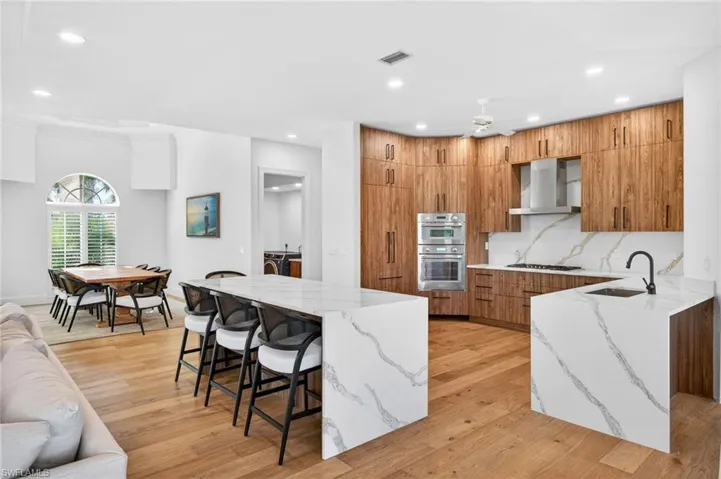 Kitchen featuring light stone counters, brown cabinets, a breakfast bar, open floor plan, and wall chimney exhaust hood